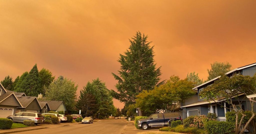 Residential neighborhood street illuminated by a glowing orange sky filled with wildfire smoke.